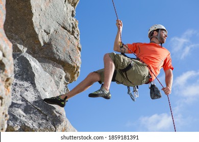 Low angle shot of a male rock climber descending down a rock face using a rappelling rope. - Powered by Shutterstock