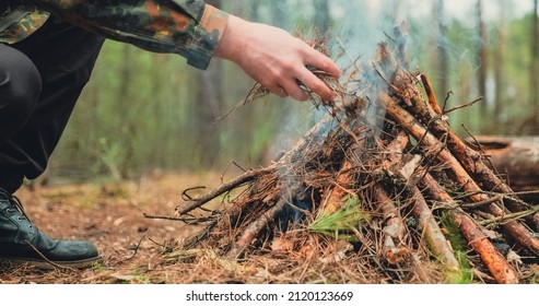 Low angle shot of a man is trying make a fire in the forest. Close-up of a man's hand lighting a campfire. Lighting a fire in the forest by a person. Low angle of a burning fire made of brushwood.