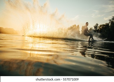 Low angle shot of man wakeboarding on a lake. Man water skiing at sunset. - Powered by Shutterstock