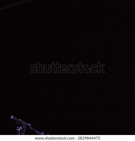 A low angle shot of a microphone stand and microphone against a dark background in an indoor environment with low light and subtle highlights on the metallic and plastic surfaces.
