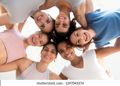 Low Angle Shot Of Multiracial Excited Girls Stand In Circle Hugging Looking At Camera At Training Together, Happy Sportive Women Embrace At Yoga Class Showing Team Spirit And Unity. Friendship Concept