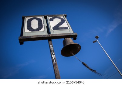 A Low Angle Shot Of An Old Flip Clock On A Metal Pole And A Big Metal Bell Hanging From It