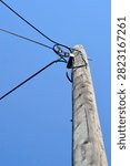 A low angle shot of an old weathered wooden utility pole with power cables connected to a junction box under a clear blue sky.