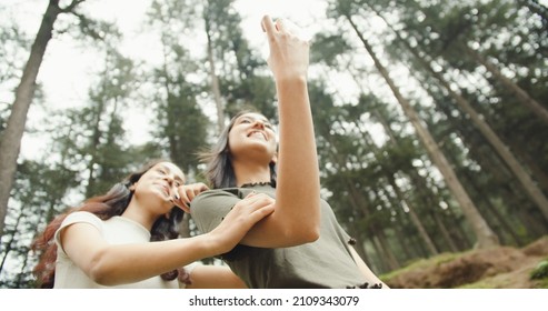 A Low Angle Shot Of A Pair Of Young Indian Female Friends Taking A Selfie In A Park