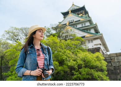 low angle shot portrait of happy asian girl photographer enjoying breeze and looking into distance with magnificent Osaka castle at background in japan - Shutterstock ID 2223706773