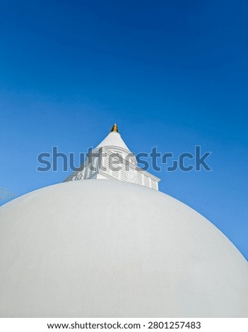 Low angle shot of a pristine white Buddhist stupa (dagoba) towering into a clear blue sky, capturing architectural simplicity and spirituality.