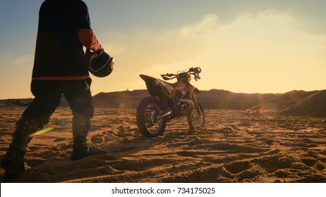 Low Angle Shot of the Professional Motocross Driver Getting Ready to Ride His FMX Dirt Bike on the Quarry Sand Terrain.