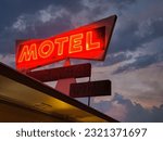 A low angle shot of red neon motel sign against dark cloudy sky background