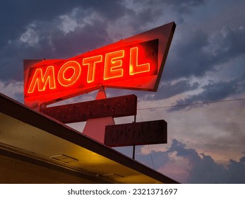 A low angle shot of red neon motel sign against dark cloudy sky background