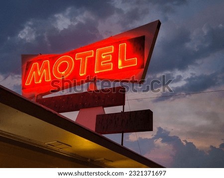 A low angle shot of red neon motel sign against dark cloudy sky background