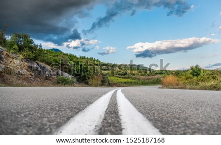 Low angle shot of road and green hills with blue sky and clouds.