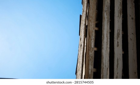 Low angle shot of rustic weathered wooden planks with peeling paint against a vibrant clear blue sky. Ample copy space on the left side for text or presentation background.
Old aged wooden wall panels viewed from below, juxtaposed against a bright blue sky. Vintage architectural detail featuring natural wood texture and clear sky backdrop.