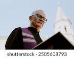 Low angle shot of senior Caucasian pastor reading Bible at funeral