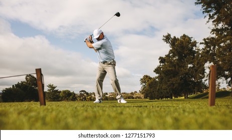 Low angle shot of senior male golfer taking shot while standing on field. Full length of golf player swinging golf club. - Powered by Shutterstock