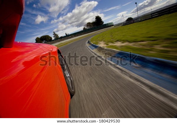 Low angle shot\
from the side of a car driving in a curve in a racetrack. Red car\
running in a racetrack.
