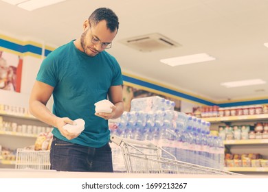 Low Angle Shot Of Smiling Man Holding Products From Freezer. Handsome Bearded Guy Shopping In Grocery Store. Shopping Concept