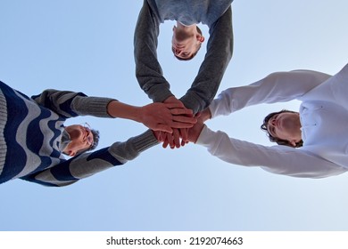 A Low Angle Shot Of Three Young Friends Putting Their Hands Together Against A Blue Sky