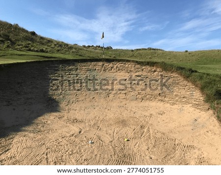 Low angle shot of two golf balls in a steep sand trap with green hills
