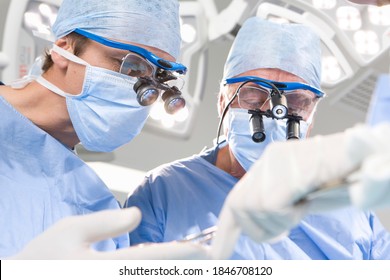 A Low Angle Shot Of Two Surgeons Attentively Performing An Operation Wearing A Surgical Loupe