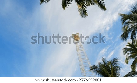 Low angle shot of a white watchtower or lighthouse structure surrounded by coconut palm trees against a blue sky at Tanjung Ular.