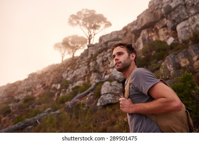 Low Angle Shot Of A Young Male Hiker On A Nature Trail With The Misty Mountain Top And Trees Behind Him