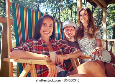 Low angle side shot of happy and positive company of people posing at the camera while sitting on comfortable summer beach chairs. Woman sitting on her man's knees