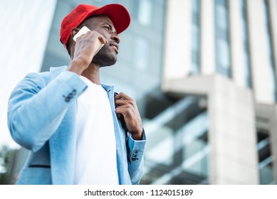 Low Angle Side View Beaming Male Tourist Speaking By Mobile While Walking At Street. Copy Space