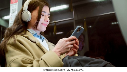 Low angle side view of cute beautiful young woman travelling by bus listening to music chatting online with smartphone. Pretty caucasian female smiling enjoying ride in empty public transport.