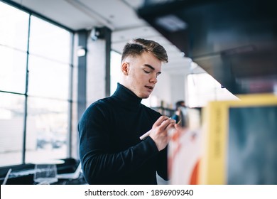 Low angle side view of pensive male student with creative hairstyle writing with pencil while standing near bookcase in library behind large window - Powered by Shutterstock