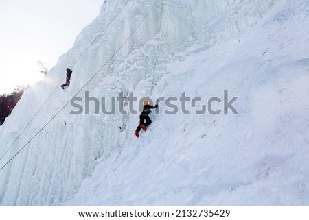 Low angle side view of two ice climbers on steep frozen cliff seen during a beautiful sunny winter day in the Montmorency Falls Park, Quebec City, Quebec, Canada