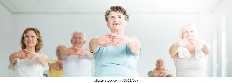 Low Angle Of Smiling Elderly Woman Stretching With A Group Of Senior People In A Yoga Center