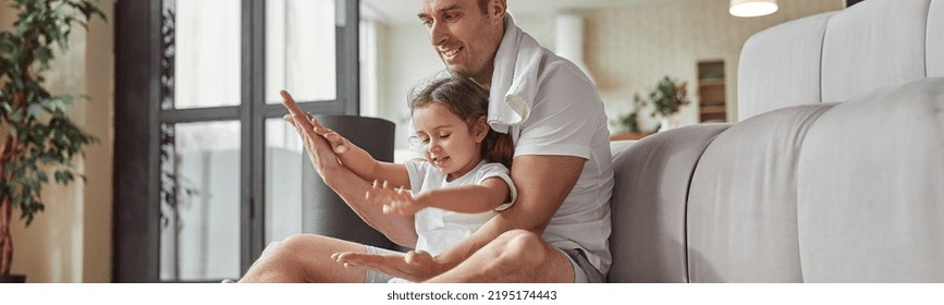 Low Angle Of Smiling Man With Little Girl Sitting On Floor In Living Room And Having Fun