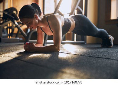 Low angle of smiling pretty female standing in plenk position on elbows while training in studio