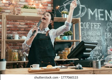 Low Angle Of Startup Business Woman Owner In Cafe Store Enjoy Music In Counter. Carefree Asian Korean Waitress Standing And Dancing While Singing With Bread Tongs In Coffee Shop After Prepared Order.