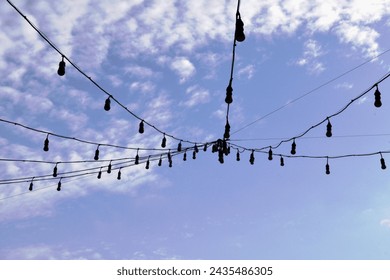a low angle of the strings of small lights at thin wires against a backdrop of bright blue sky and dramatic white clouds