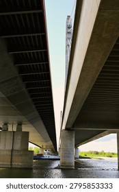 Low angle symmetrical view underneath the modern concrete concrete highway bridges spanning across the Waal river near Andelst and Ewijk, infrastructure engineering in Netherlands