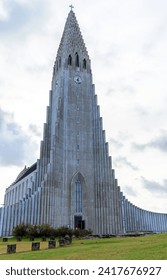 Low angle of tall Hallgrimskirkja Lutheran parish church with large building structure and with stepped concrete facade on green ground in Reykjavik Iceland under cloudy blue sky