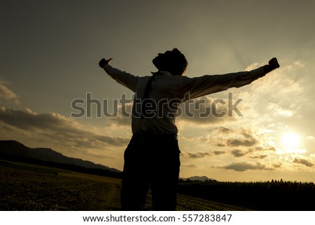 Low angle three quarter body view of silhouetted person with spread arms in countryside sunset, freedom concept.