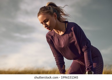 Low angle of tired young fit female in sportswear leaning on knees and breathing heavily after intense running workout in summer field