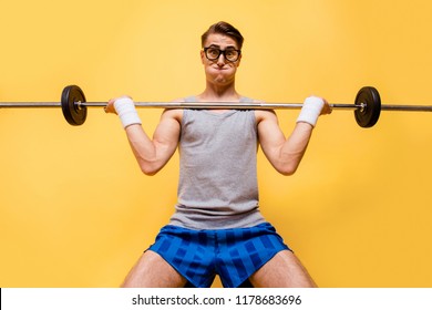 Low angle top view portrait of youngster joke, comic man push hard weight barbell up isolated on shine yellow background