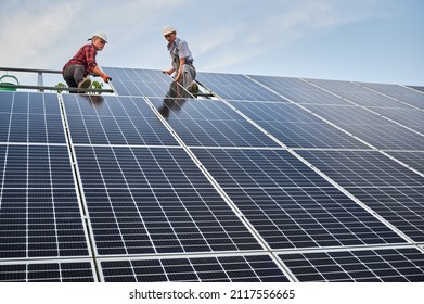 Low angle of two men solar technicians building photovoltaic solar panels under blue sky. Male workers in safety helmets placing solar module on metal rails. Concept of alternative energy sources. - Shutterstock ID 2117556665