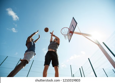 Low angle  of two young men playing basketball and jumping by hoop against blue sky, copy space - Powered by Shutterstock