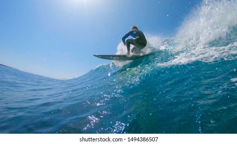 LOW ANGLE, UNDERWATER, LENS FLARE: Male Surfboarder Riding And Carving Cool Barrel Wave Near A Volcano. Fit Sportsman Surfing Ocean Waves In The Canary Islands. Active Tourist Having Fun On Surfboard.