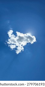 Low angle vertical shot of a single white cloud blocking the sun on a bright blue sky with a glowing edge effect