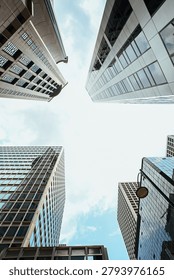 Low angle vertical view of modern glass facade skyscrapers reaching towards cloudy sky in financial business district center of Hong Kong