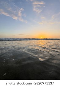 Low angle vertical view of rippling ocean water facing a bright pinpoint sun at sunset in Carlsbad, California.