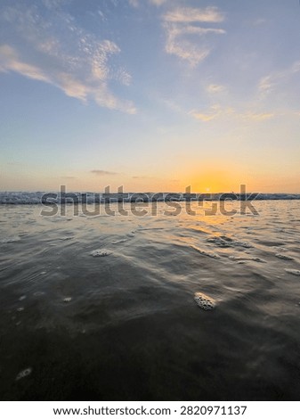 Low angle vertical view of rippling ocean water facing a bright pinpoint sun at sunset in Carlsbad, California.