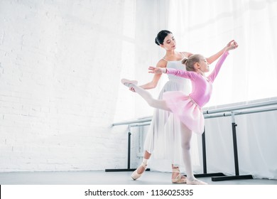 Low Angle View Of Adult Ballerina Training With Child In Pink Tutu In Ballet Studio