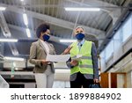 Low angle view of African American company manager communicating with quality control inspector who is visiting woodworking production facility during COVID-19 pandemic.