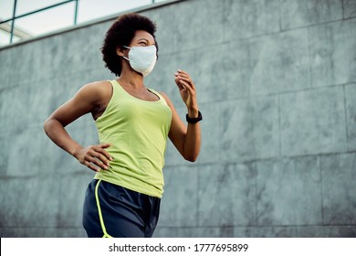 Low Angle View Of African American Sportswoman With Protective Face Mask Running In The City. Copy Space.